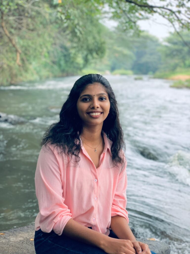 A woman in a pink shirt sits on a rock by a river, representing a digital marketing freelancer in Kerala enjoying nature.