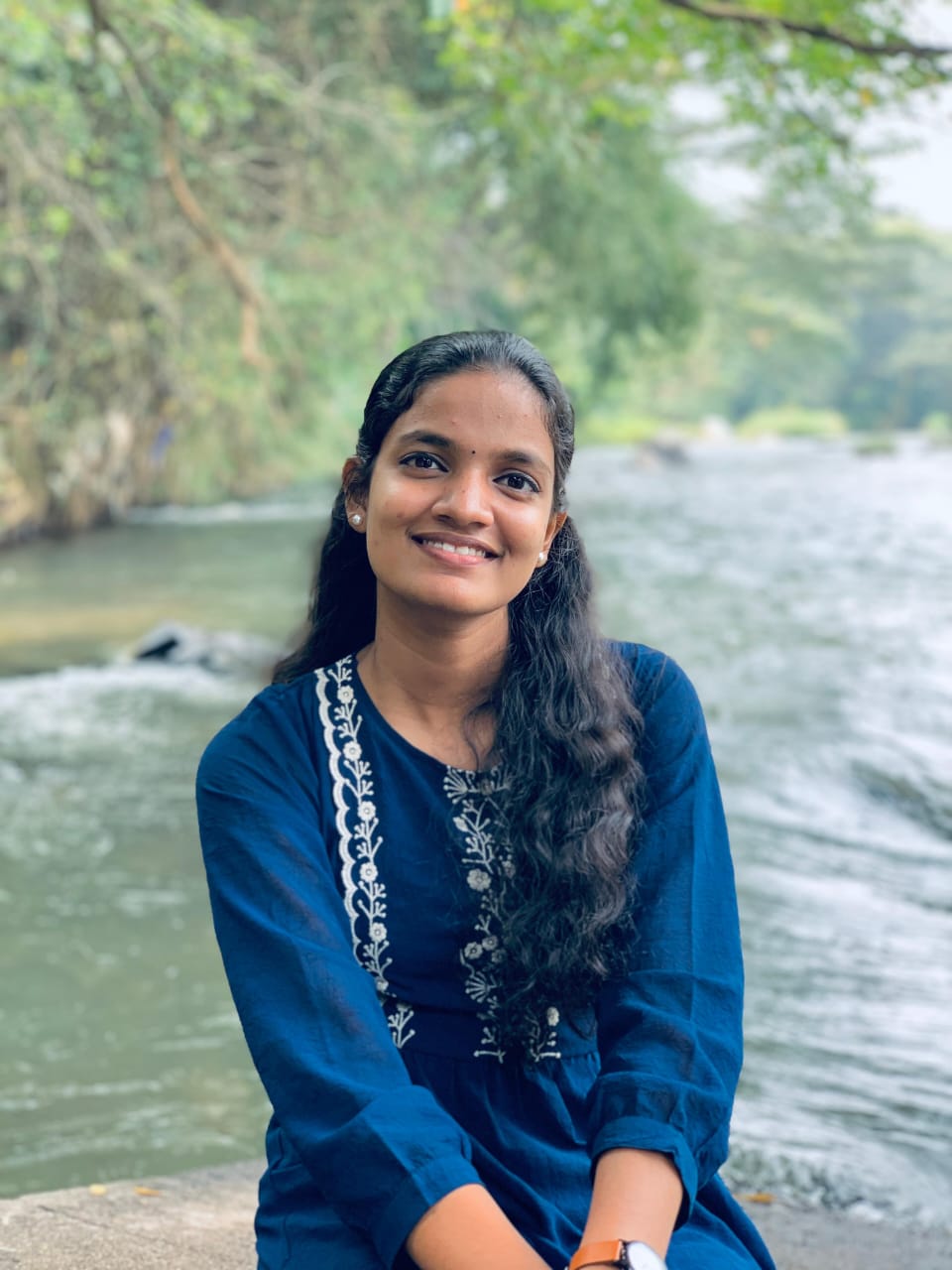 A young woman sits on a rock by a river, reflecting on her work as a digital marketing freelancer in Kerala.